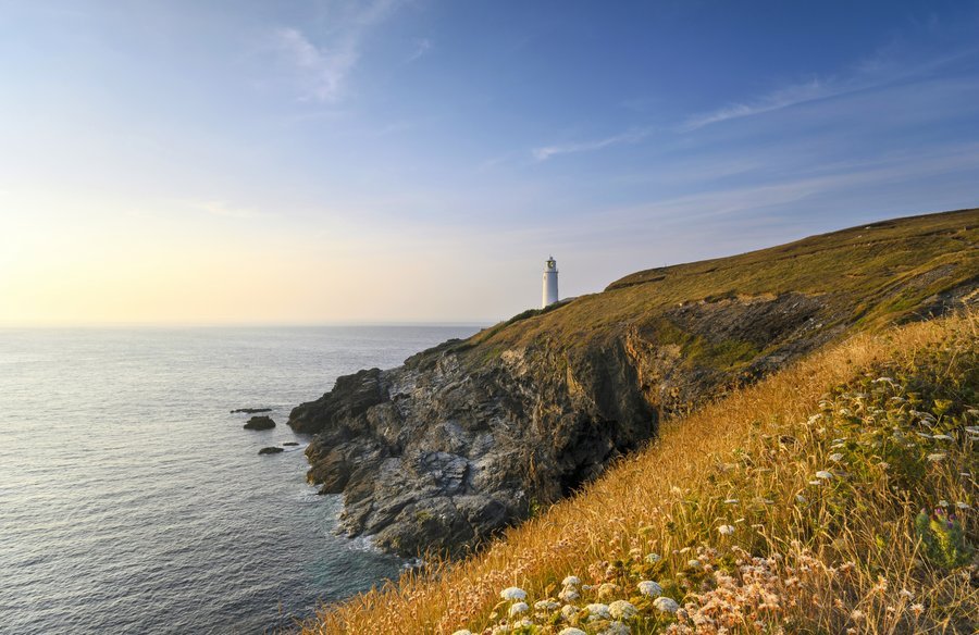 A clifftop path above the sea, a lighthouse on the headland beyond