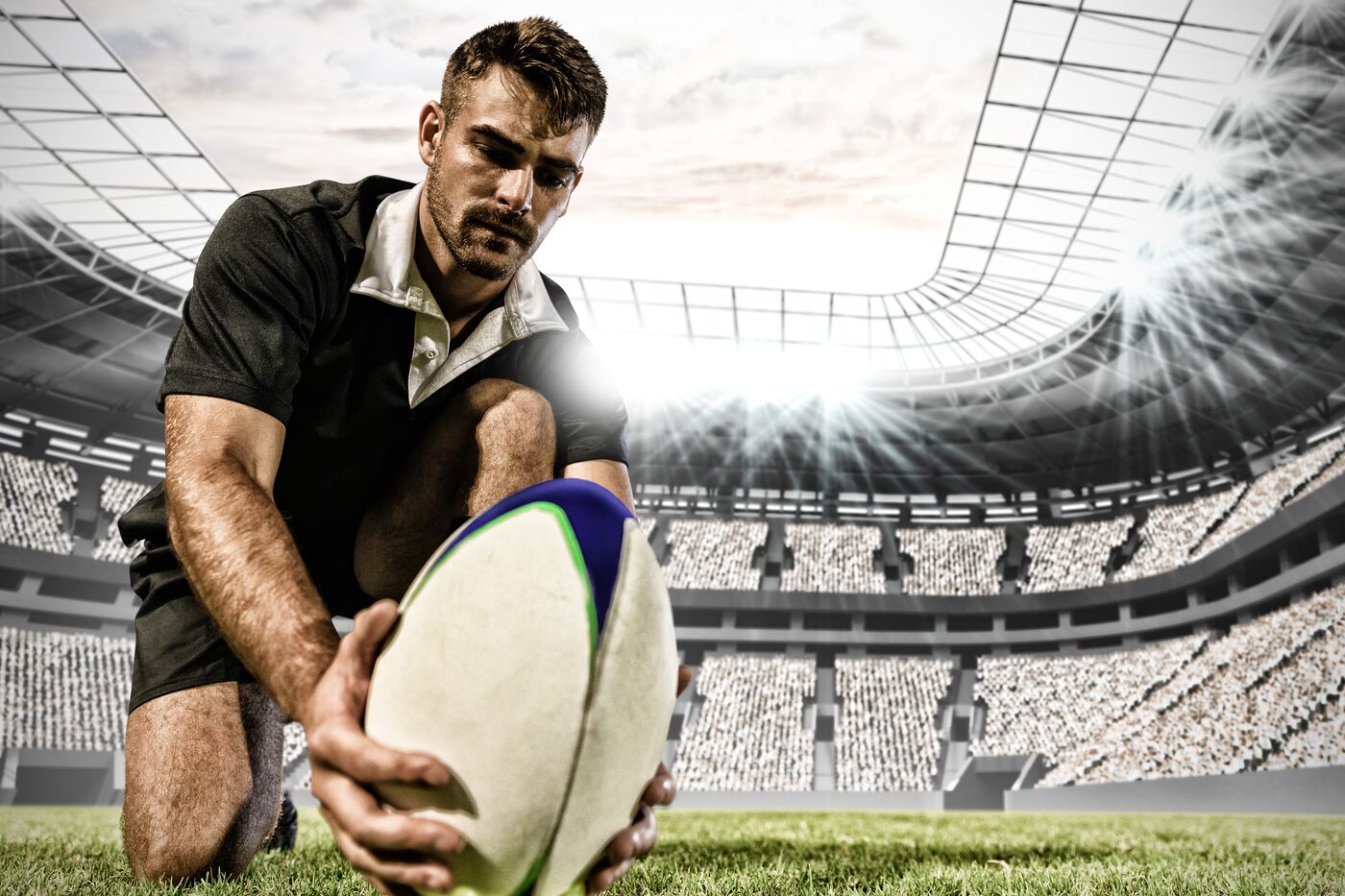 A rugby player kneeling to set the ball for a kick in a stadium