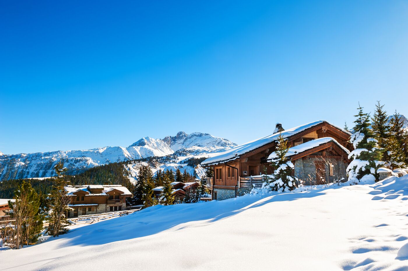 A wooden chalet in deep snow with mountains on the horizon