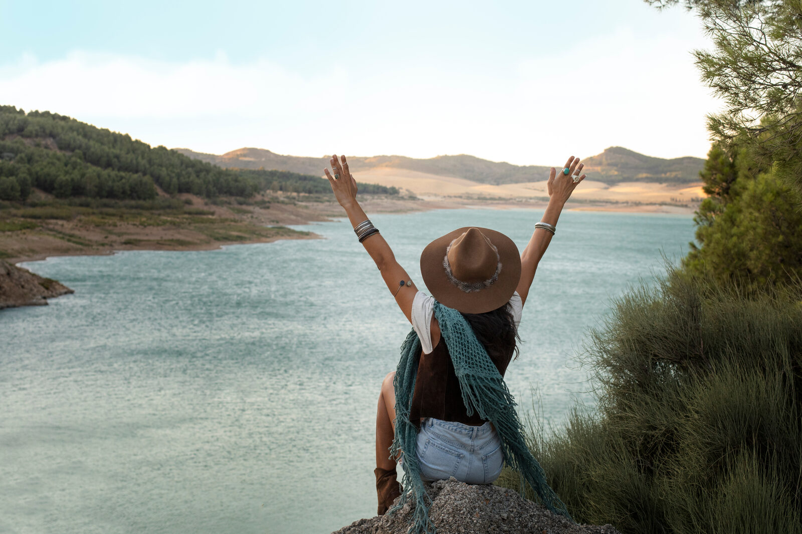 A lone traveller with arms raised above a wide valley