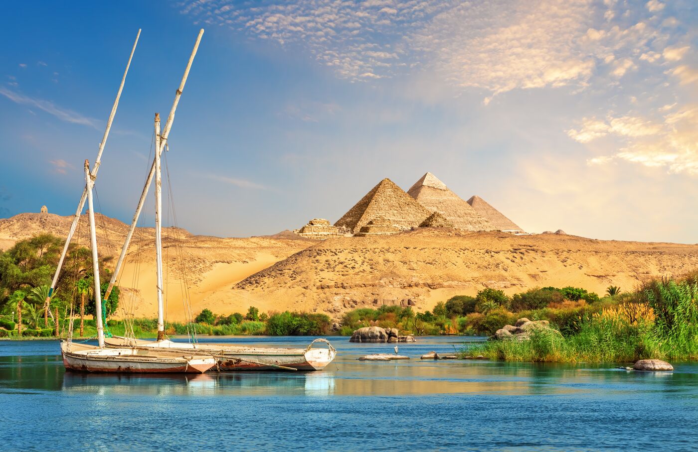 Sailboats moored on the Nile with pyramids in the desert beyond
