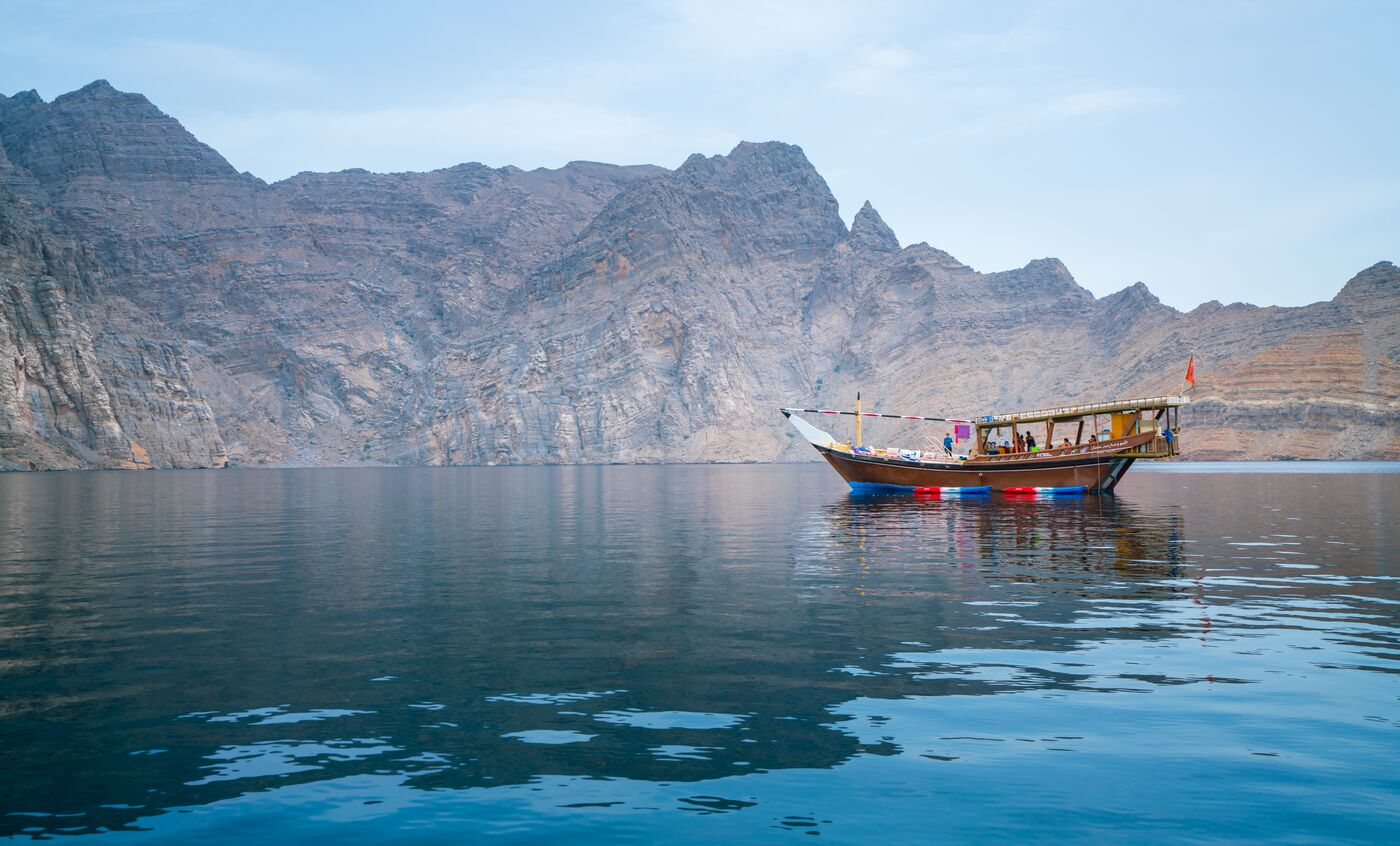 A wooden dhow on still water below bare mountains