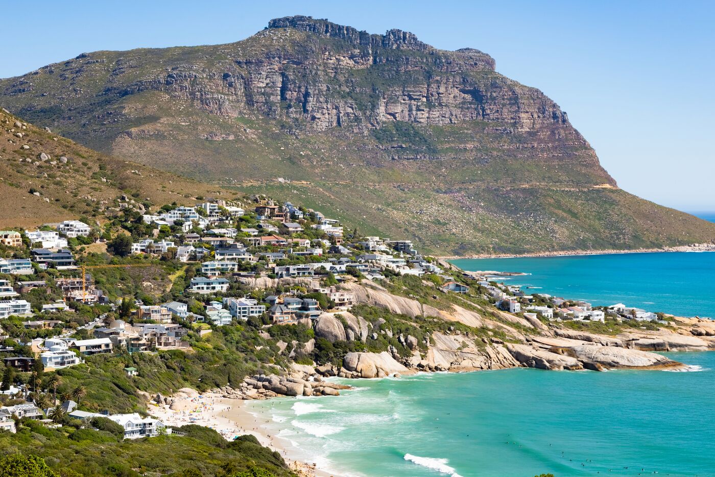 Houses on a green hillside above a turquoise bay below a mountain
