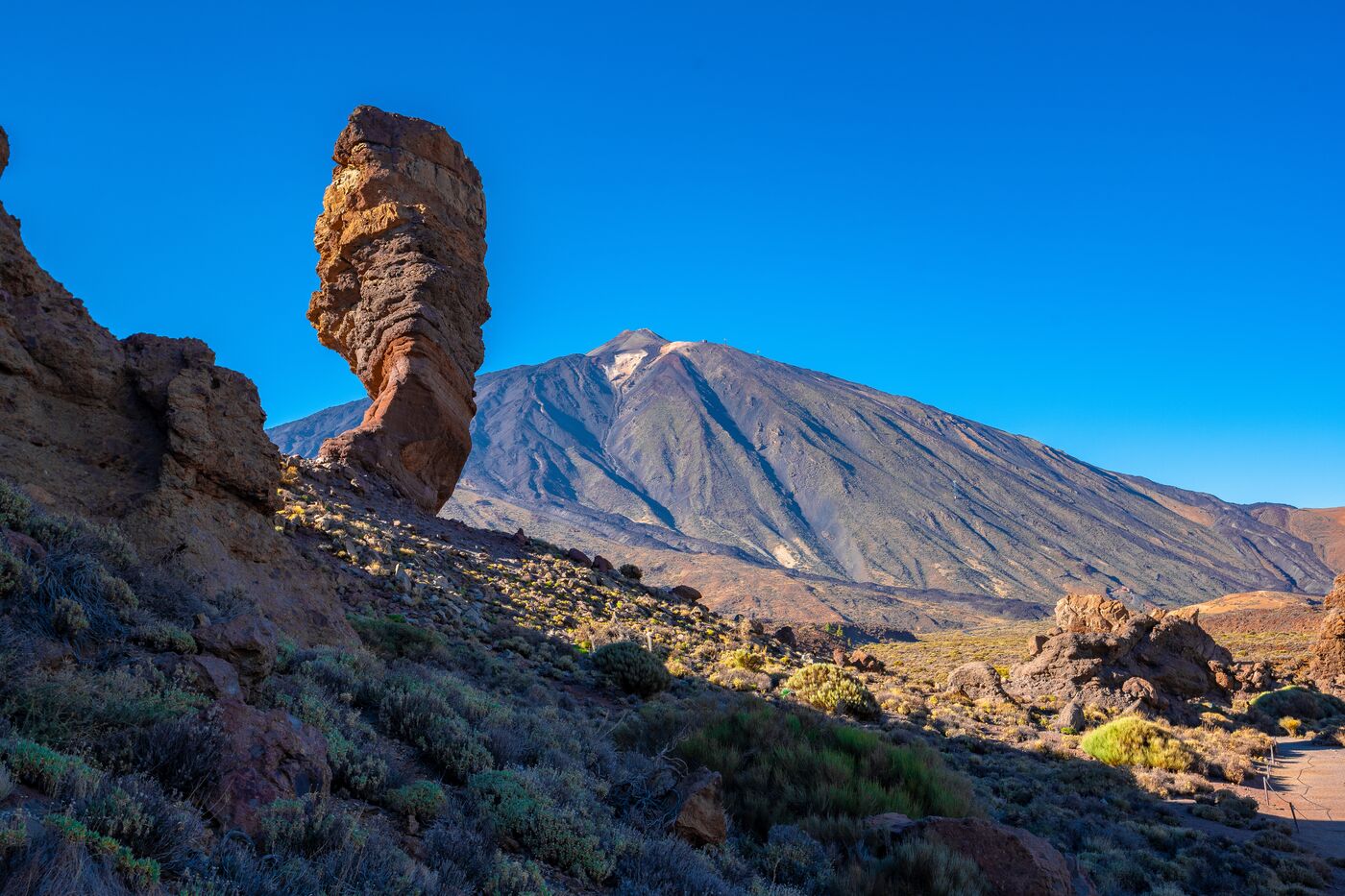 A tall rock pillar in front of Mount Teide under a blue sky