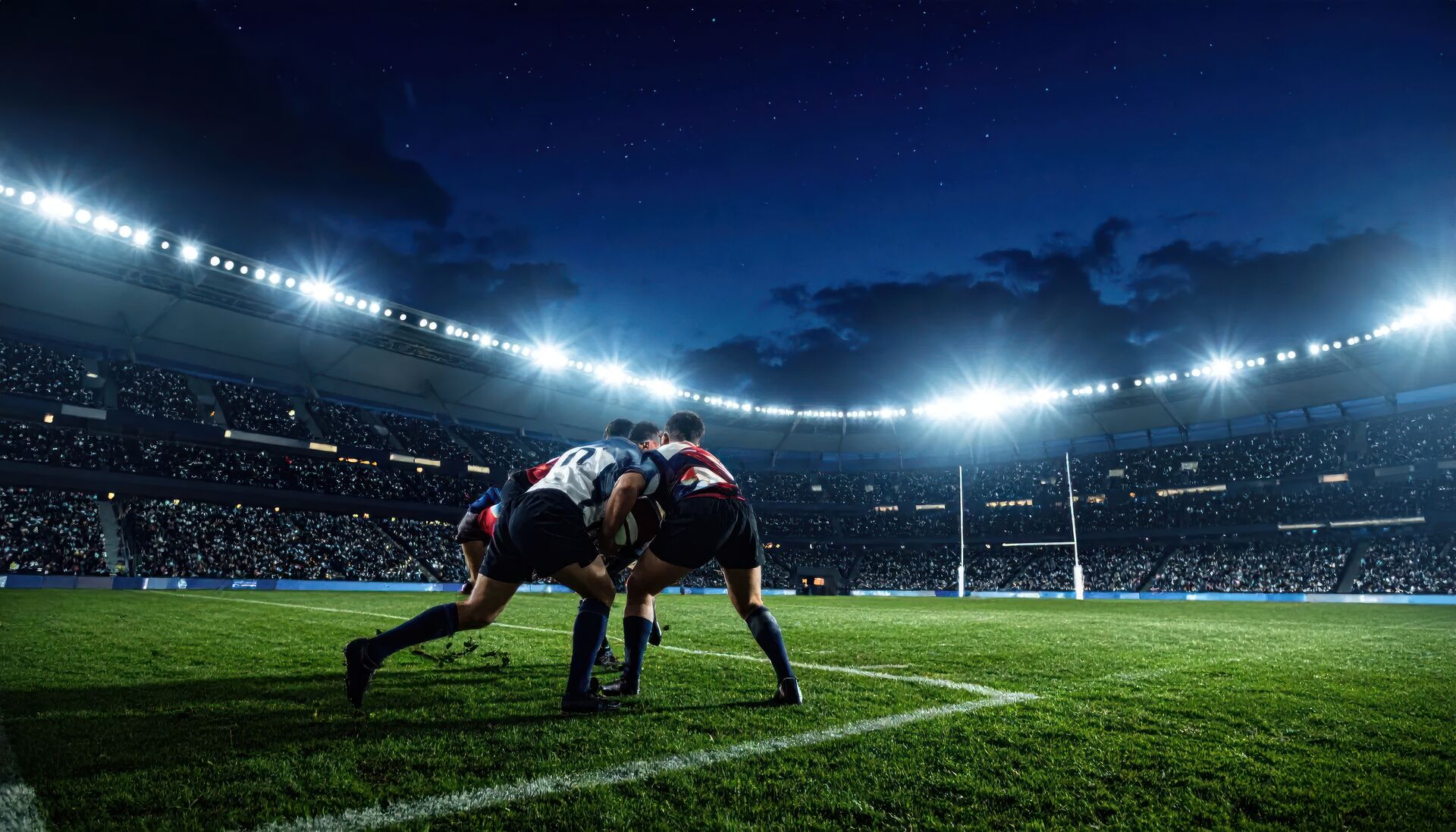 Two rugby players contesting the ball in a floodlit stadium at night