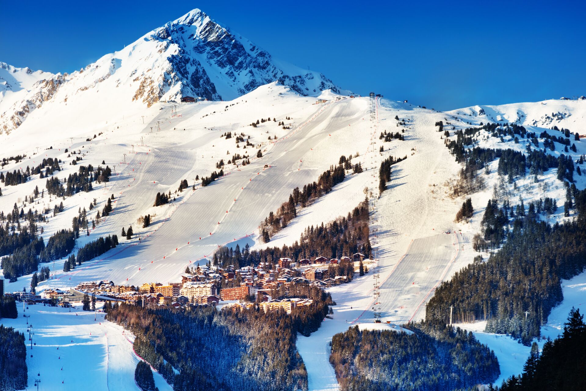 A ski village below a snow-covered peak, with pistes cut through the forest