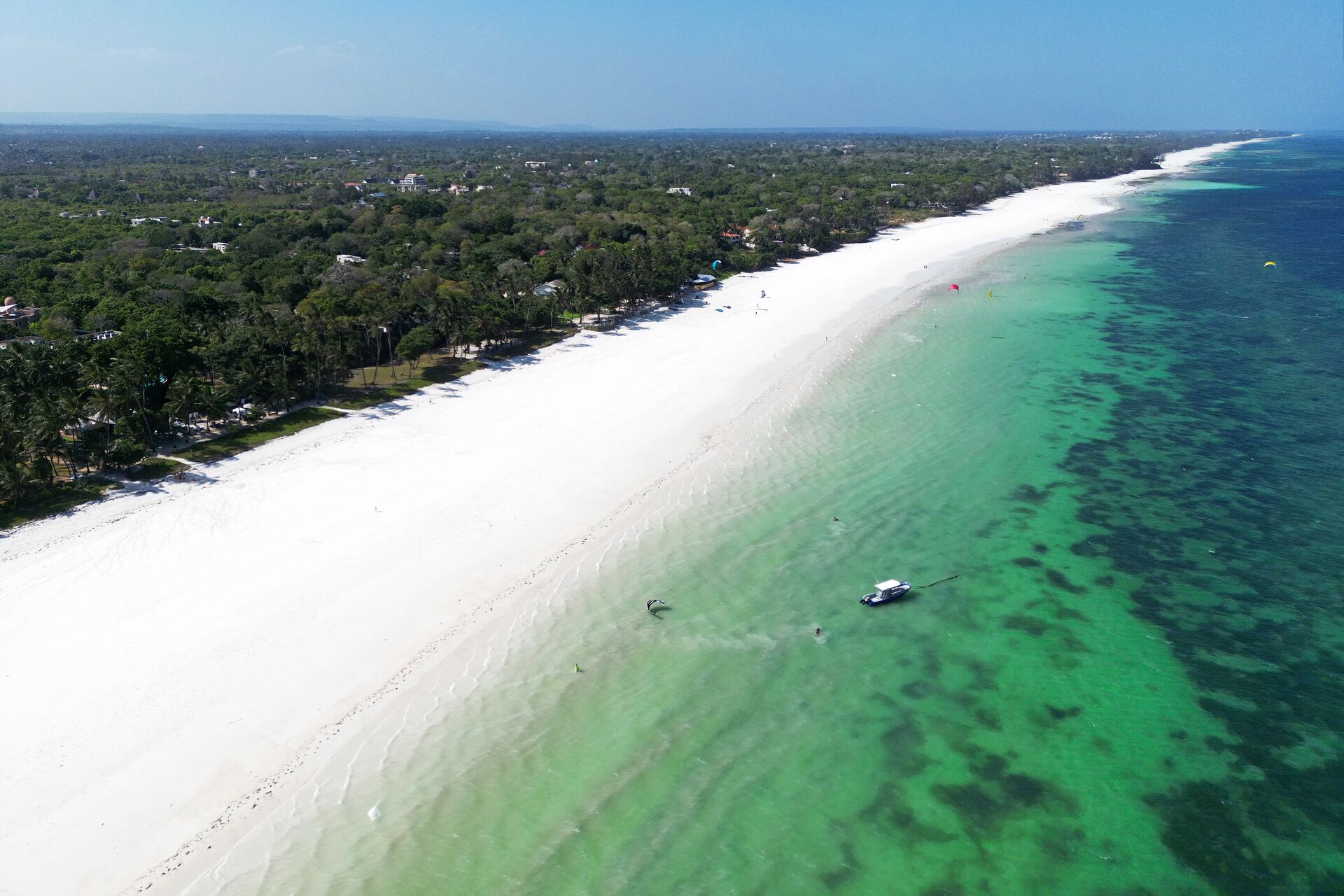 A long white beach beside turquoise water, seen from above